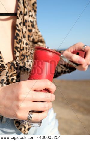 Compact Red Manual Coffee Grinder In Female Hands Close Up. On Nature, Sea Background. Barista Girl