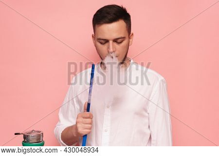 A Male Model Smokes A Hookah, Sheesha And Enjoys It. Pink Background
