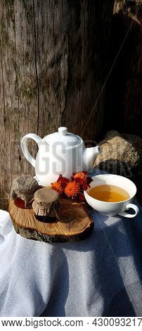 Healthy Chamomile Tea Poured Into White Cup. Teapot, Small Honey Jar, Heather Bunch And Glass Jar Of