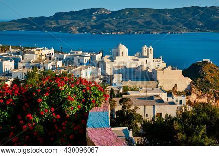 Picturesque scenic view of Greek town Plaka on Milos island over red geranium flowers and Orthodox greek church. Plaka village, Milos island, Greece