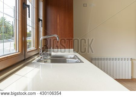 Metal Faucet In Modern Kitchen With White Granite Top Illuminated By Large Window With Outside View