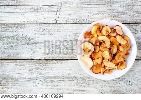 A Pile Of Dried Apples In Slices On A White Plate On Wooden Background. Dried Fruit Chips. Healthy F