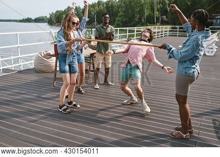 Friends cheering for young man bending backwards to walk under vertical bar playing limbo