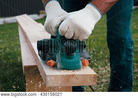 Carpenter Hands In Gloves Electric Plane Planing Lumber, Flying Shavings, Sawdust. Close-up On Glove