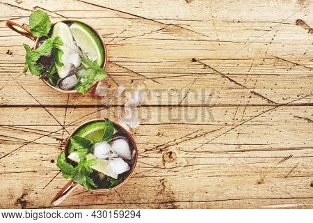 Moscow Mule Cocktails In Copper Mug With Lime, Ice, Ginger Beer, Vodka And Mint. Wooden Background, 