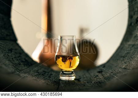 A glass of whiskey in old oak barrel. Copper alambic on background. Traditional alcohol distillery concept