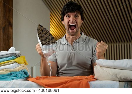 Young Man Ironing Clothes At Home Angry And Mad Screaming Frustrated And Furious, Shouting With Ange