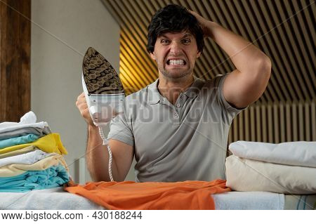 Young Man Ironing Clothes At Home Angry And Mad Screaming Frustrated And Furious, Shouting With Ange