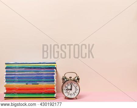 A Stack Of Colorful Notebooks And An Alarm Clock On The Table. A Horizontal Frame With Space. Pastel
