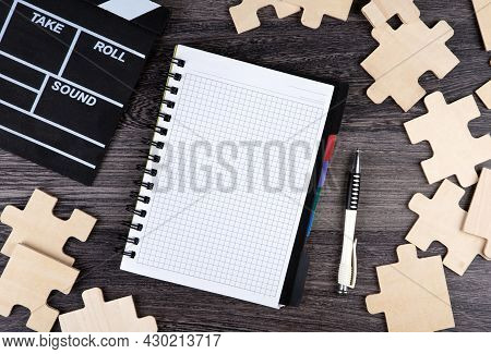 Notepad With Cinematic  Clapper, Pen And Puzzle Pieces On A Table Top View