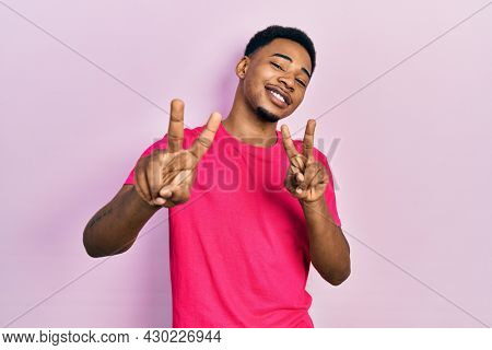 Young african american man wearing casua t shirt smiling looking to the camera showing fingers doing victory sign. number two. 