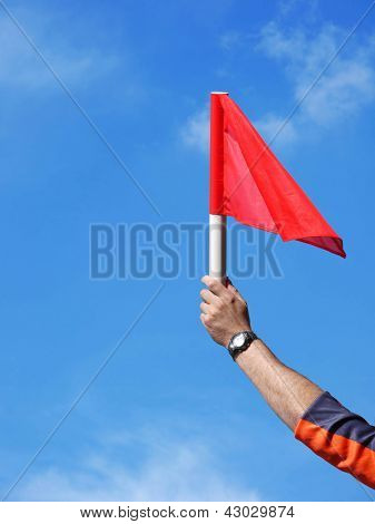 Main d'arbitre assistant football brandissant son drapeau rouge sur le ciel bleu signalisation hors-jeu