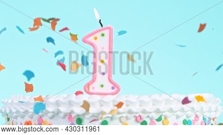 Colorful tasty birthday cake with candles shaped like the number 1. Pastel blue background.