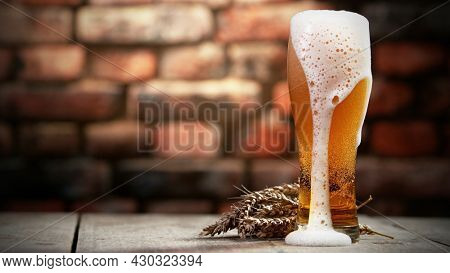 Glass of beer with foam spilling over the edge. Served in stylish old brick wall interior.