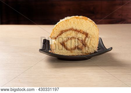 Rocambole, Slice Of Roacambole Stuffed With Sweet Bed On A Black Plate On A Table. Dark Background, 