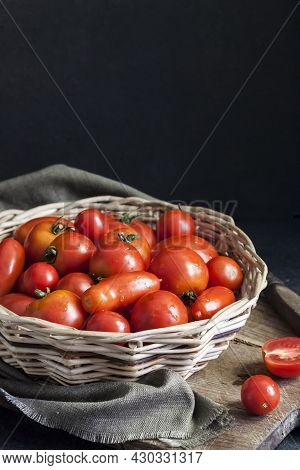 Fresh Red Tomatoes In Whicker Basket On Black Background. Copy Space