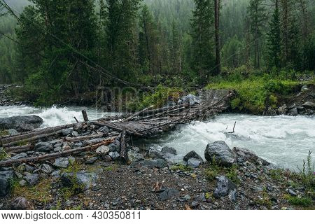 Atmospheric Rainy Landscape With Forest And Bridge Over Mountain River. Dark Forest Scenery With Pow