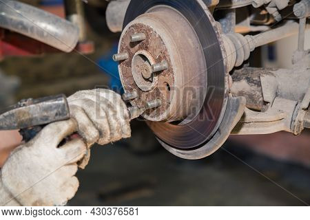 Hands Knock Off The Thread On The Bolt Of The Worn Rear Hub With A Hammer. In The Garage, A Person C