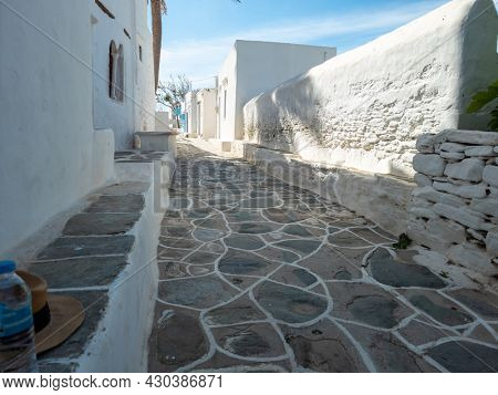 Exploring the empty narrow cobblestone streets between whitewashed buildings of Sifnos island Kastro town Greece necessary accessories are hat and bottle of water. Summer famous destination Cyclades.