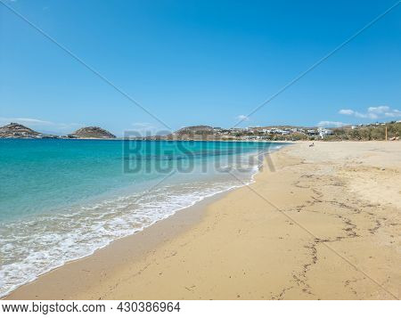 Golden sandy tropical beach at famous cosmopolitan Mykonos island, Cyclades Greece. Buildings, clear blue sky, transparent calm sea background. Space, summer holidays card and advertisement template.