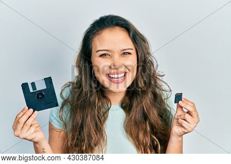 Young hispanic girl holding floppy disk and sdxc card smiling and laughing hard out loud because funny crazy joke. 