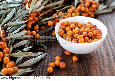 Branch Of Seabuckthorn Berries With Bottle Of Oil At  Wooden Background
