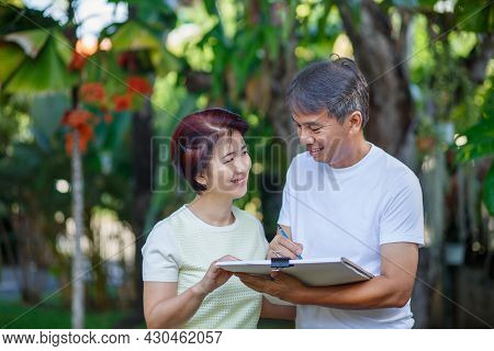 Asian Middle-aged Couple Talking And Designing Garden Plan Together In Backyard.