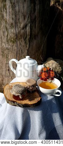 A Cup Of Tea And A Teapot On A Wooden Stand With Jars Of Honey And Flowers On A White Tablecloth