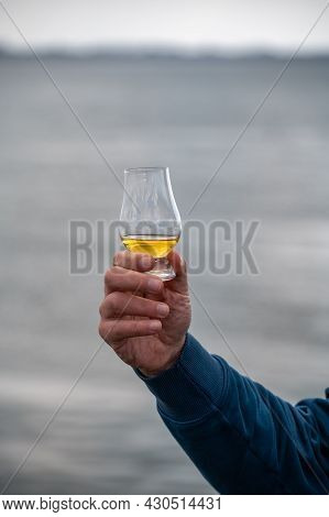 Hand Holding Dram Of Single Malt Scotch Whisky On Seashore In Scotland