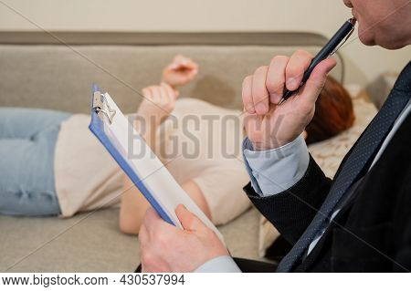 Caucasian Woman Lies On A Couch At A Reception With A Psychotherapist. An Elderly Man Works As A Psy