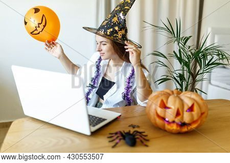Halloween Witch Hat.woman With Pumpkin And Laptop. Indoor Portrait Of Cute Young Witch At Home. Pret