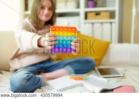 Teenage Girl Playing With Rainbow Pop-it Fidget Toy While Studying At Home. Teen Kid With Trendy Str