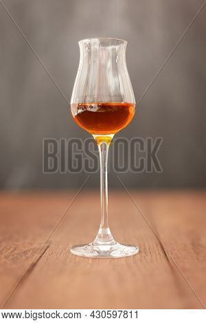 Grappa Glass With Brandy Or Sherry Or Calvados On Wooden Table With Light Grey Background.