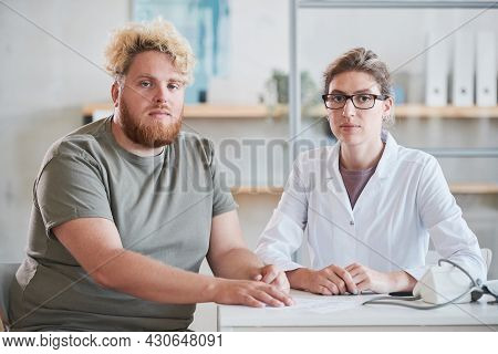 Portrait Of Young Overweight Man Sitting At The Table With His Nutritionist And They Looking At Came