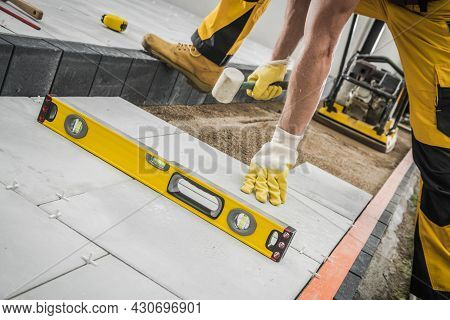 Caucasian Construction Worker With Professional Hammer In His Hand Building Concrete Tiles Pathway. 