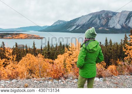 Canada travel hike tourist walking at Bove island , Tagish Lake, Yukon during Skagway road trip, Alaska. Hiker woman in green outerwaer at autumn fall mountains landscape.