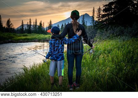Brother And Sister Standing Next To A Creek While Fishing In Alberta Canada At Sunset.