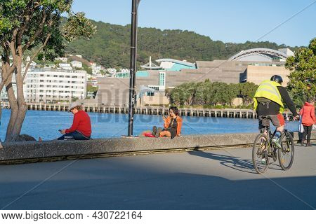 Wellington New Zealand - July 30 2021; People Using Devices Sitting On Edge Relaxing And Cycling Alo