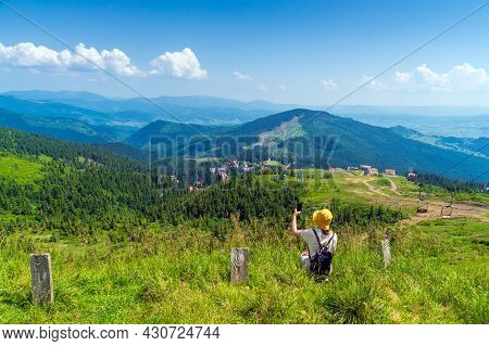 Traveler In A Hat, Resting In Nature. A Tourist Girl Photographs A Panorama Of The Mountains By A Mo
