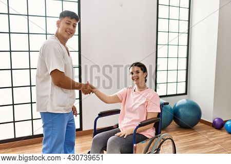 Young disabled woman and physiotherapist smiling happy shaking hands at the clinic.
