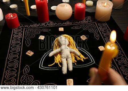 Voodoo Doll Pierced With Pins And Woman Holding Candle Above Black Mat, Closeup. Curse Ceremony