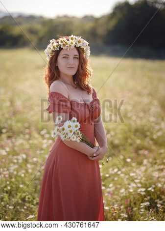 Red-haired Woman Wearing Dress And Chamomile Wreath On Field On Summer Evening. Concept Of Digital D