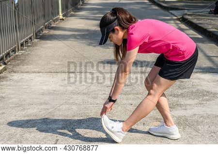 Portrait Of Runner Woman Doing Stretching And Warming Up Her Legs Before Running In The Public Park.