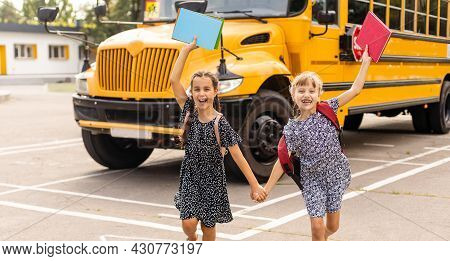 Cheerful Little Girls Next To School Bus. Backback. Back To School Concept.