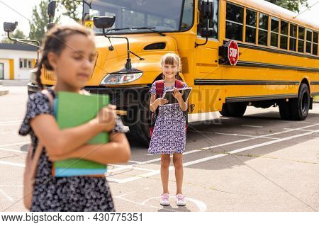 Cheerful Little Girls Next To School Bus. Backback. Back To School Concept.