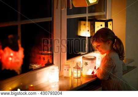 Little Kid Girl Sitting By Window With Selfmade Hand Crafted Lanterns With Candles For St. Martin Pr