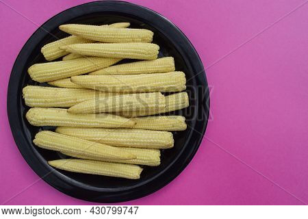Fresh And Organic Babycorn Vegetble Whole Pieces Arranged On Black Plate On Pink Solid Background Bl