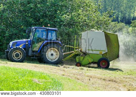 Tractor Pulling A Baler Over Lines Of Dry Cut Hay To Make Hay Bales For Animal Fodder