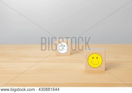 Wooden Cube With Smile Icon Face Sign. Cube With Sign Of Negative Face Icon Is Blurred In Gray Backg