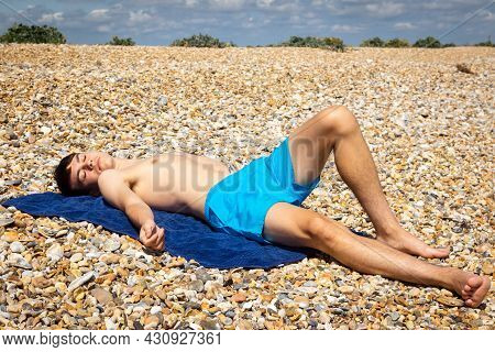 A 18 Year Old Caucasian Shirtless Teenage Boy Sunbathing On A Stoney Beach